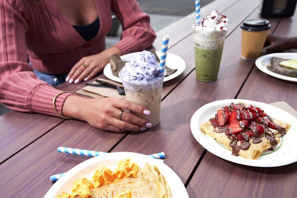 Picnic table with various crepes and a person holding a coffee drink