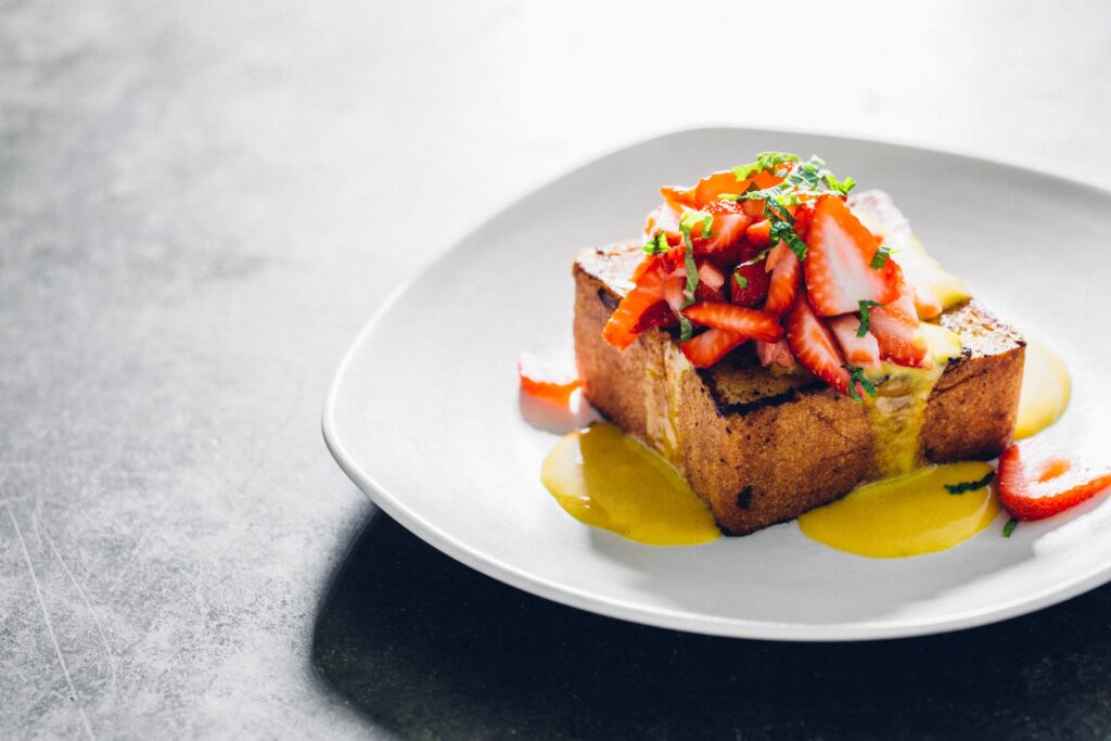 Metal table with a white plate with a large piece of bread topped with berries and mint