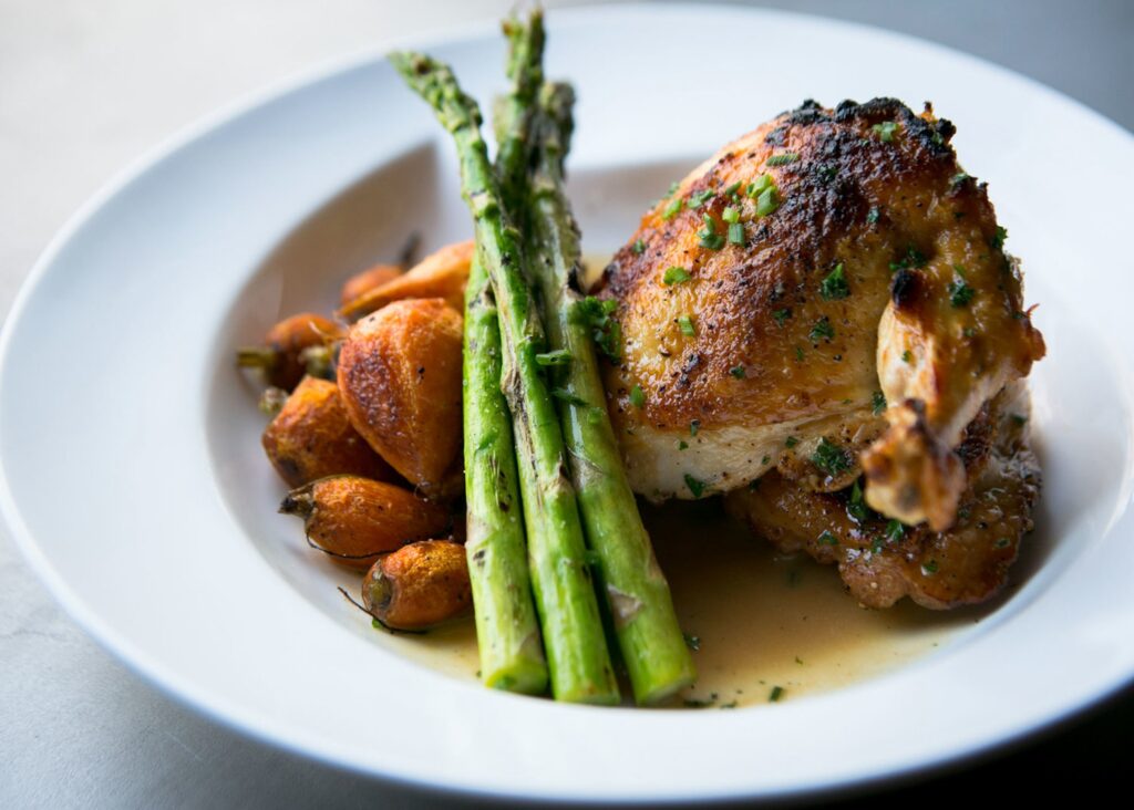 White plate with carrots, asparagus, and roast chicken pieces
