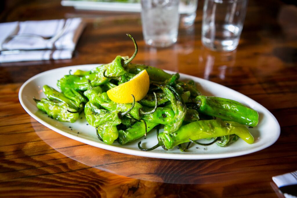 Wooden table with a white plate with green peppers and a lemon wedge
