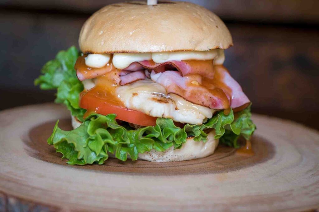 A plate with a sandwich made with grilled chicken, cheese, tomatoes, and lettuce