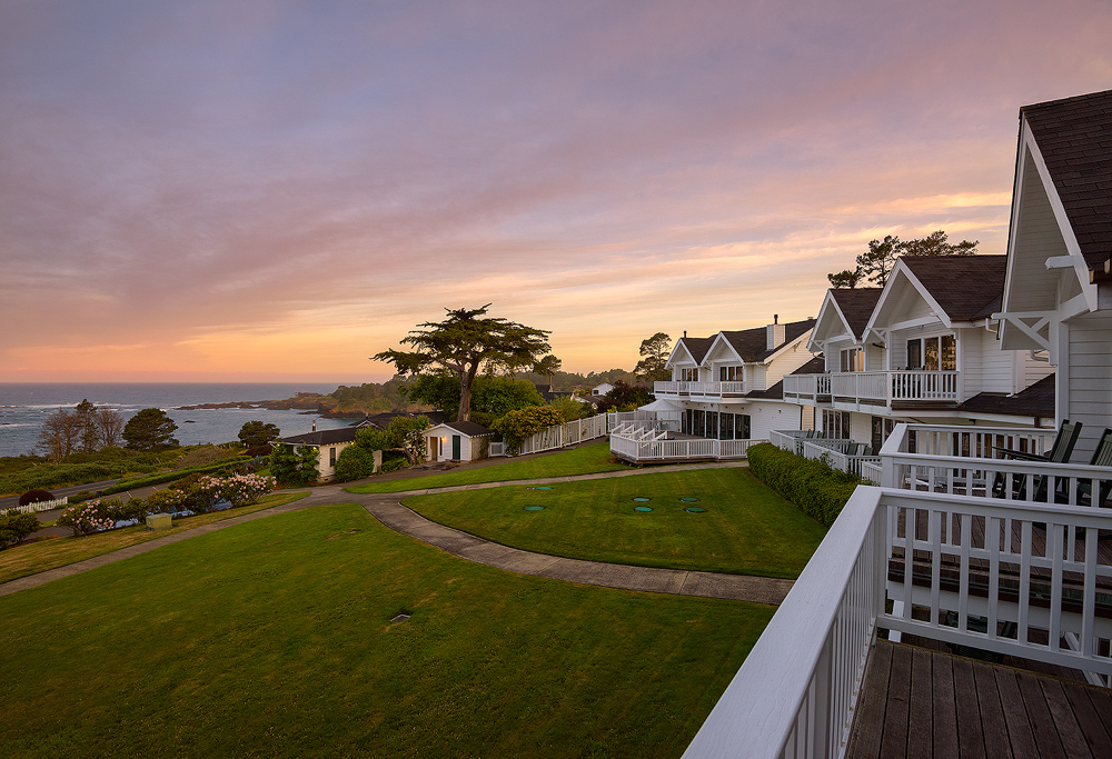 View of exterior of hotel rooms, a lawn, and the ocean at Little River Inn Mendocino California