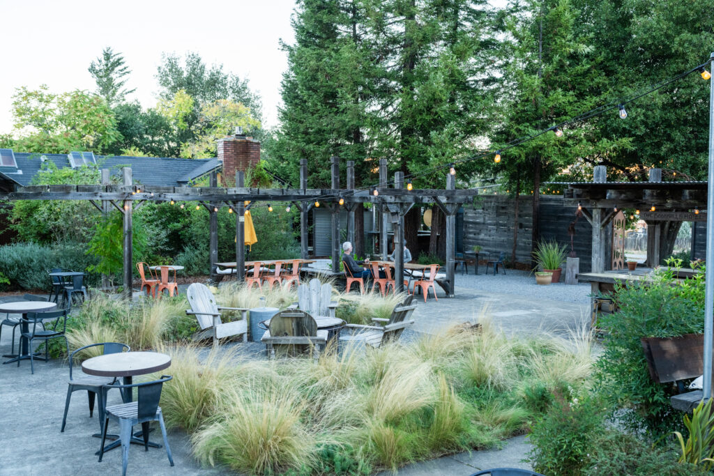 Exterior cafe garden with tables, string lights, and chairs among red wood trees
at Boonville Hotel + Restaurant