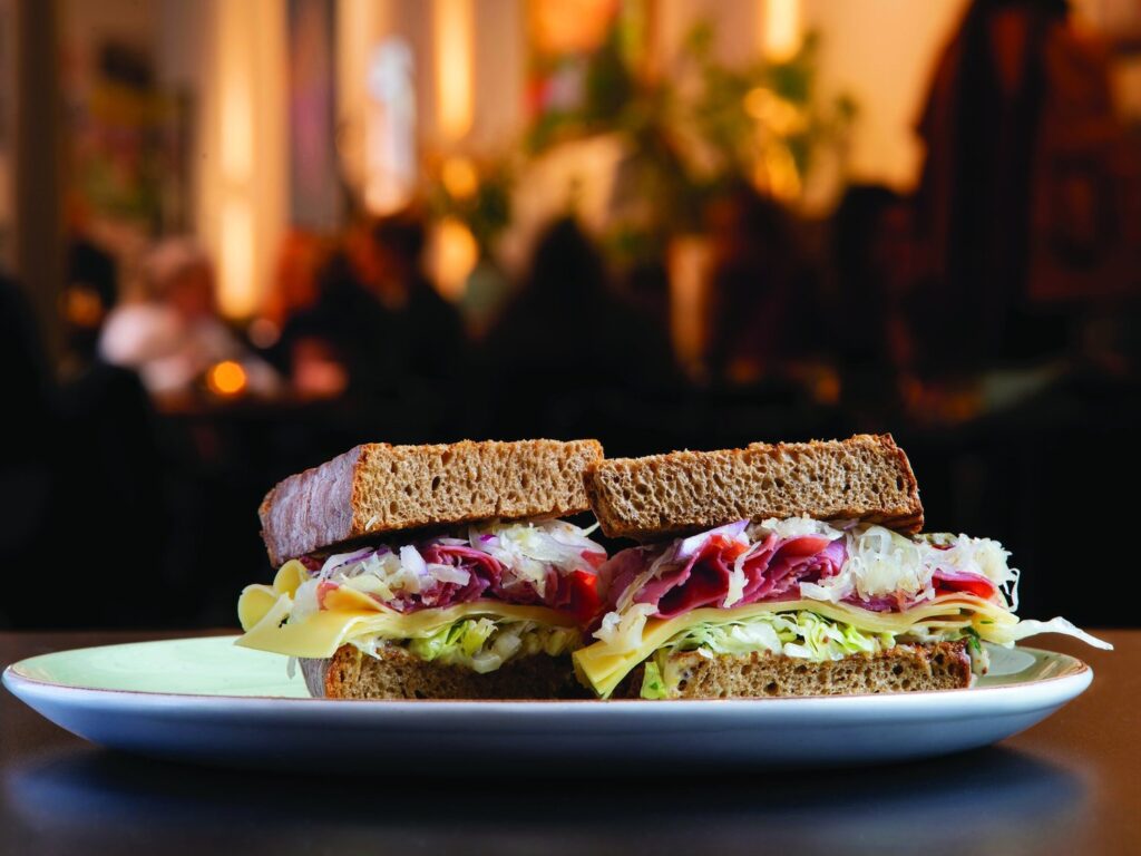 A closeup of a brown bread sandwich with cheese, greens, and meat