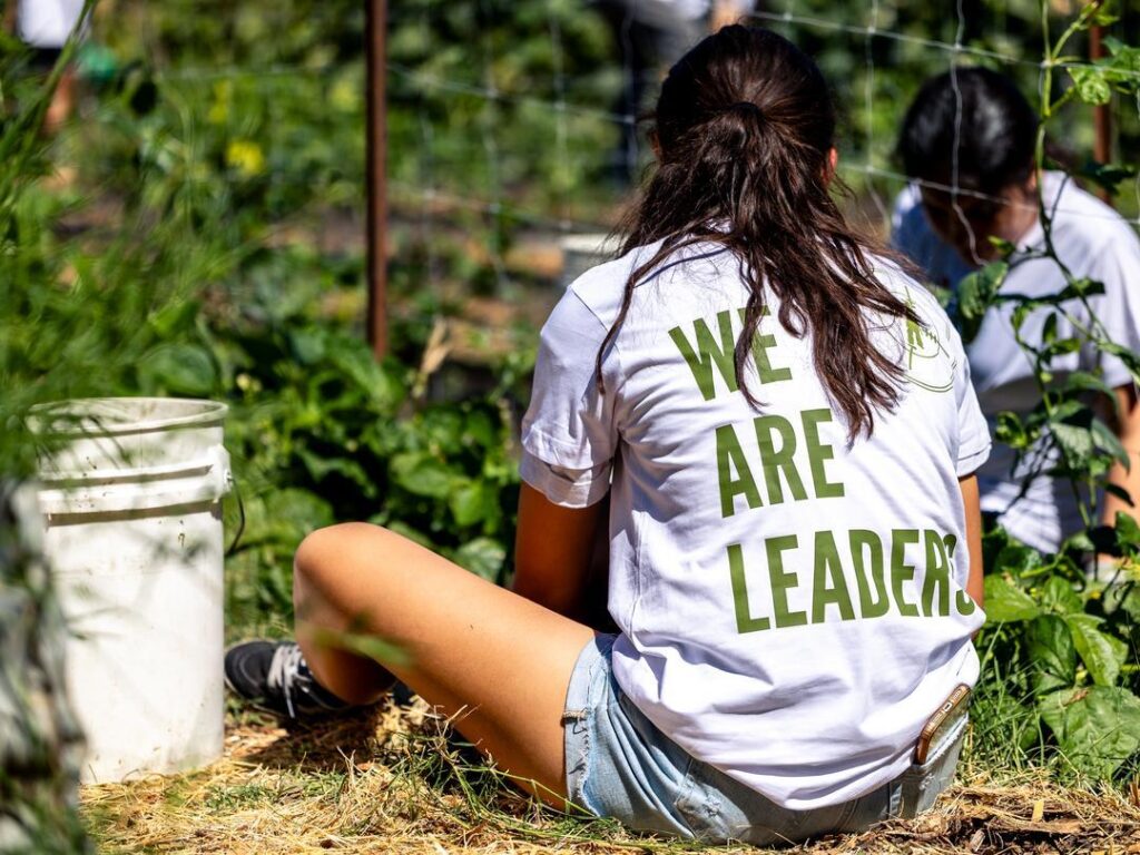 Girl sitting on the ground with tomato plants at Three Sisters Gardens, a farm near the Sierra Foothills