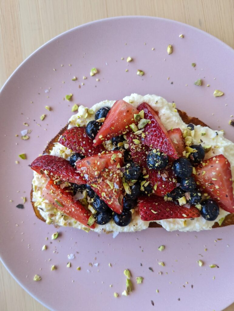 Overhead photo of a toast with ricotta, berries, and pistachios on a light purple plate