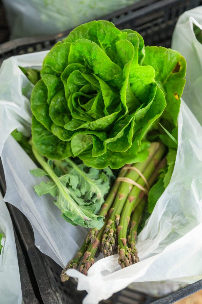 Black container with a plastic bag filled with green lettuce with asparagus