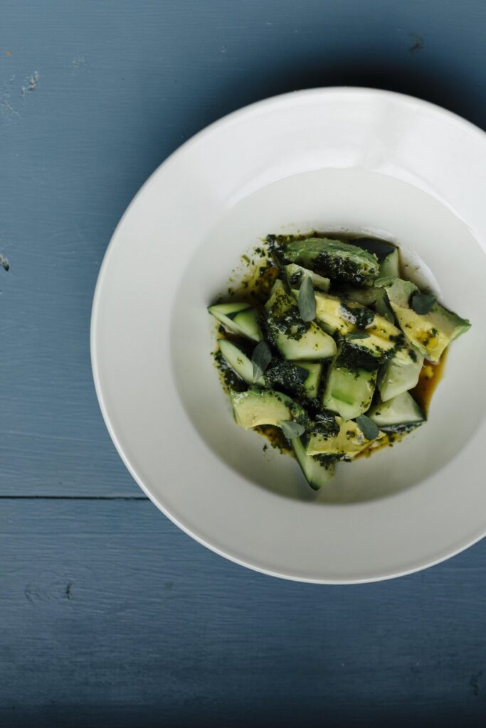 Blue table with a white plate holding cut up cucumber and avocado salad