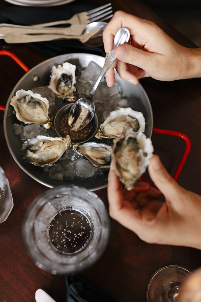 Table with a plate of oysters and a person holding an oyster