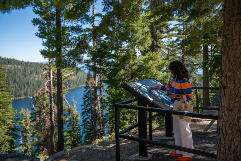 Person pointing to map with view of forest and lake in background