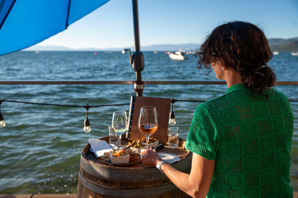 Person looking out at lake with a glass of wine and local produce