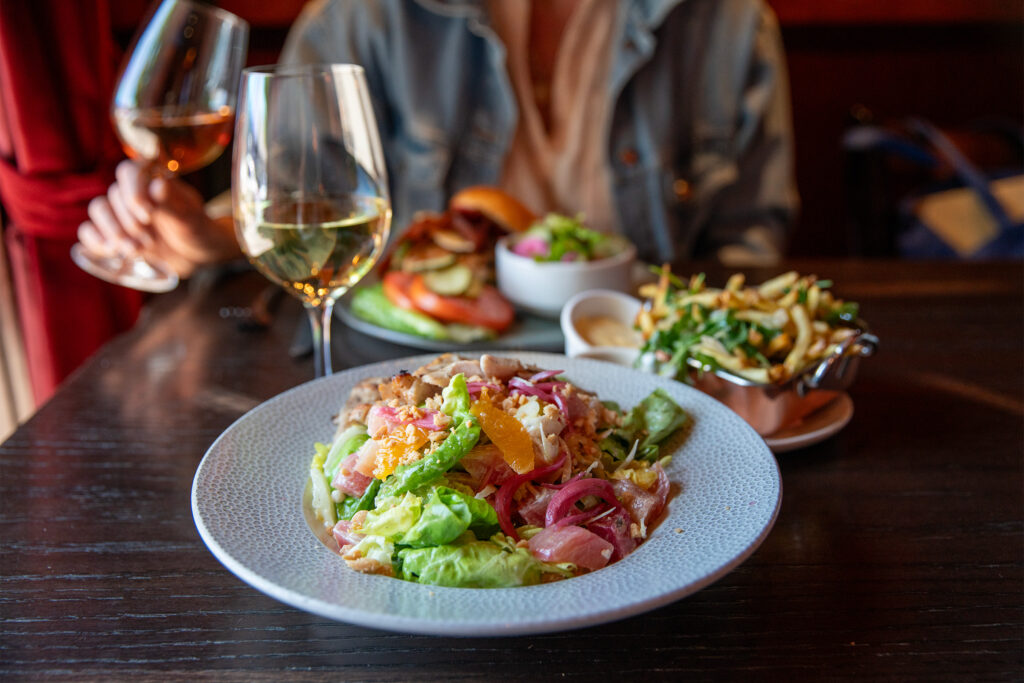 Table of food including a butter lettuce, onion, and citrus salad and glasses of wine