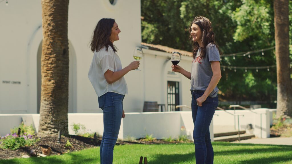 Two women talking on a lawn outside while holding wine glasses in Livermore wine country