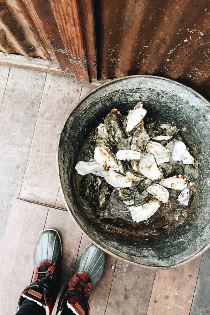 woman in boots standing next to a bucket of oysters