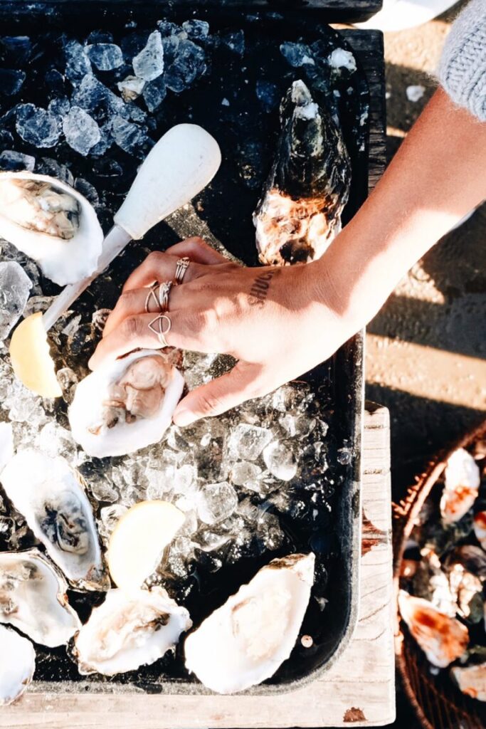 womans hand grabbing shelled oyster on ice