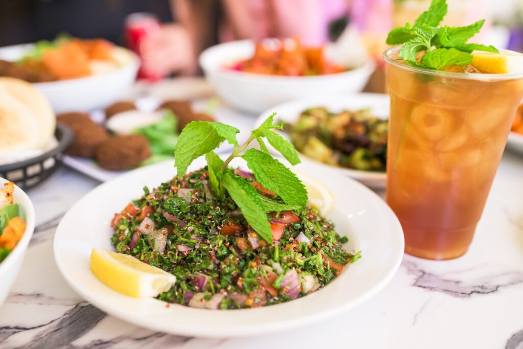 Close up of a dish of tabbouleh with a drink and other plates of food nearby