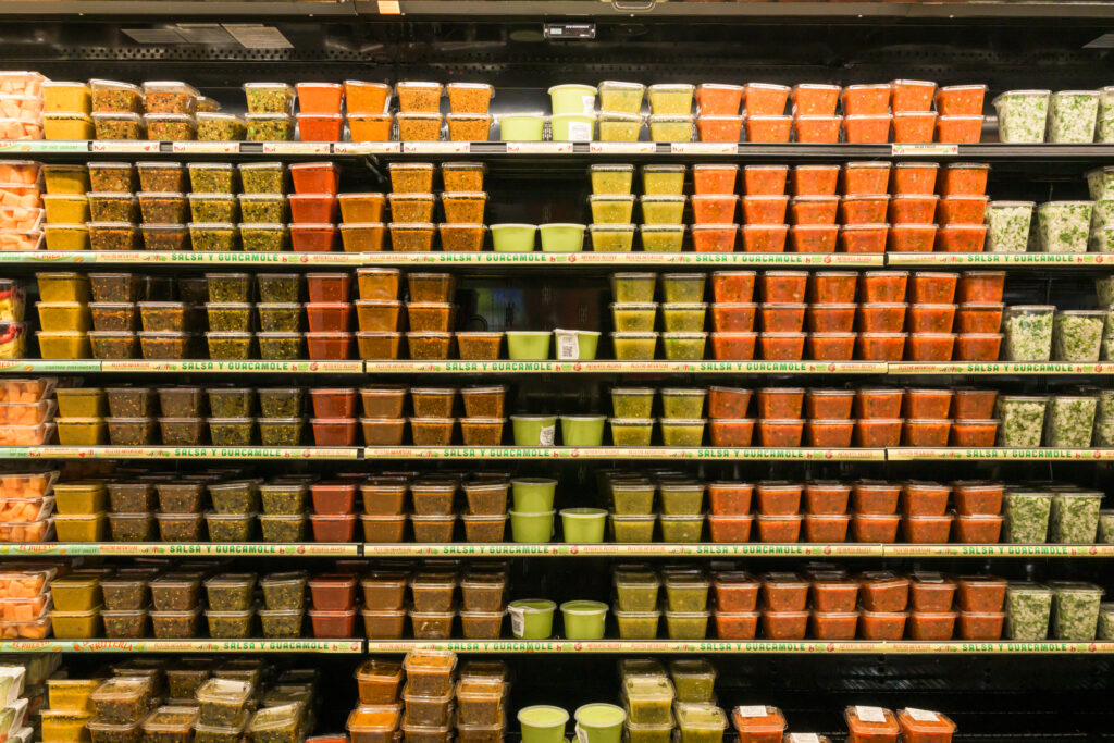 A refrigerated case filled with various salsas