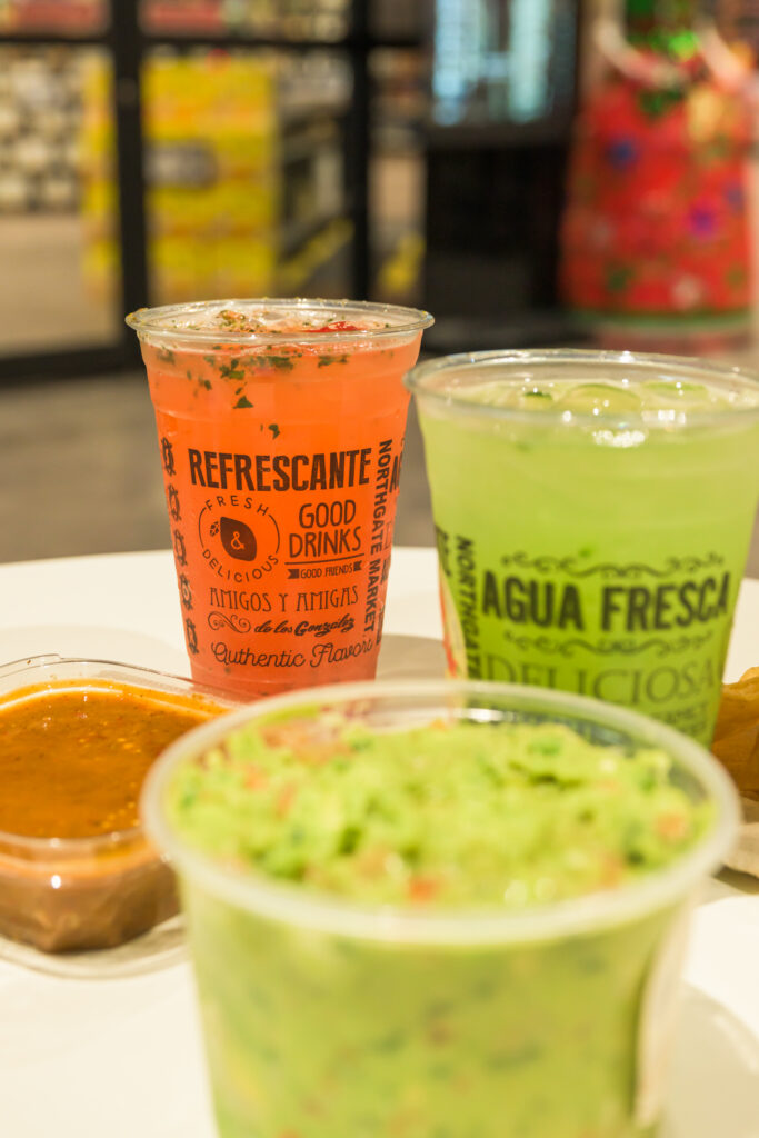 A collection of containers with guacamole, salsa, and aguas frescas